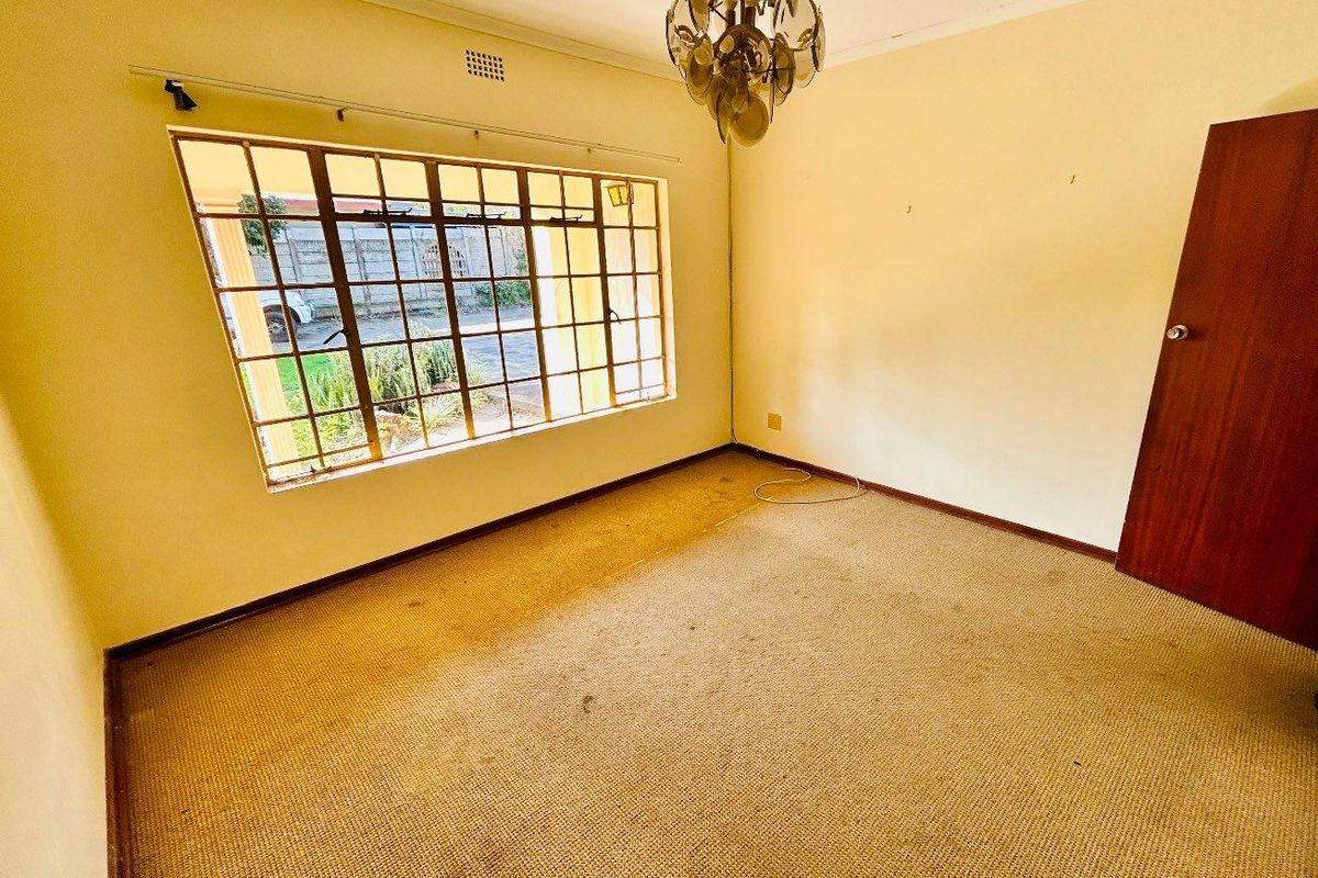 A vacant bedroom featuring large steel-framed windows, wall-to-wall carpeting, and a central ceiling light fixture.