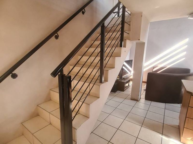 Interior hallway featuring a staircase with a metal balustrade and tiled flooring, leading into an adjacent living area.