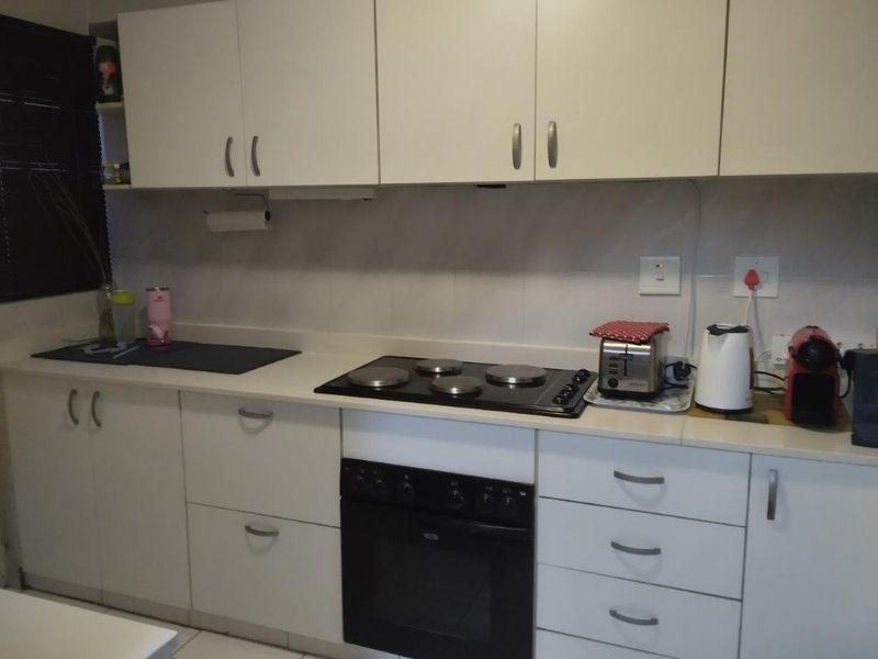A functional kitchen featuring white built-in cabinetry, a dark electric hob, a built-in oven, and a tiled backsplash with ample counter space.