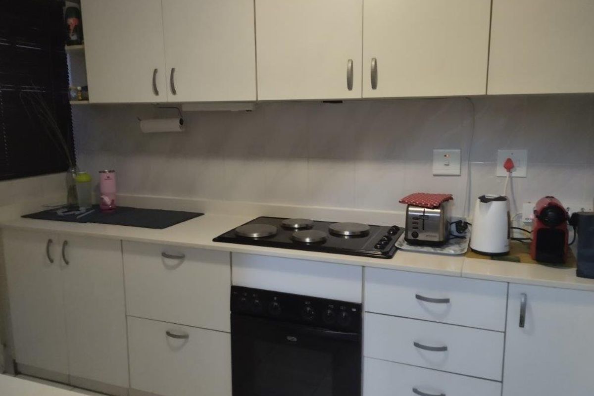 A functional kitchen featuring white built-in cabinetry, a dark electric hob, a built-in oven, and a tiled backsplash with ample counter space.
