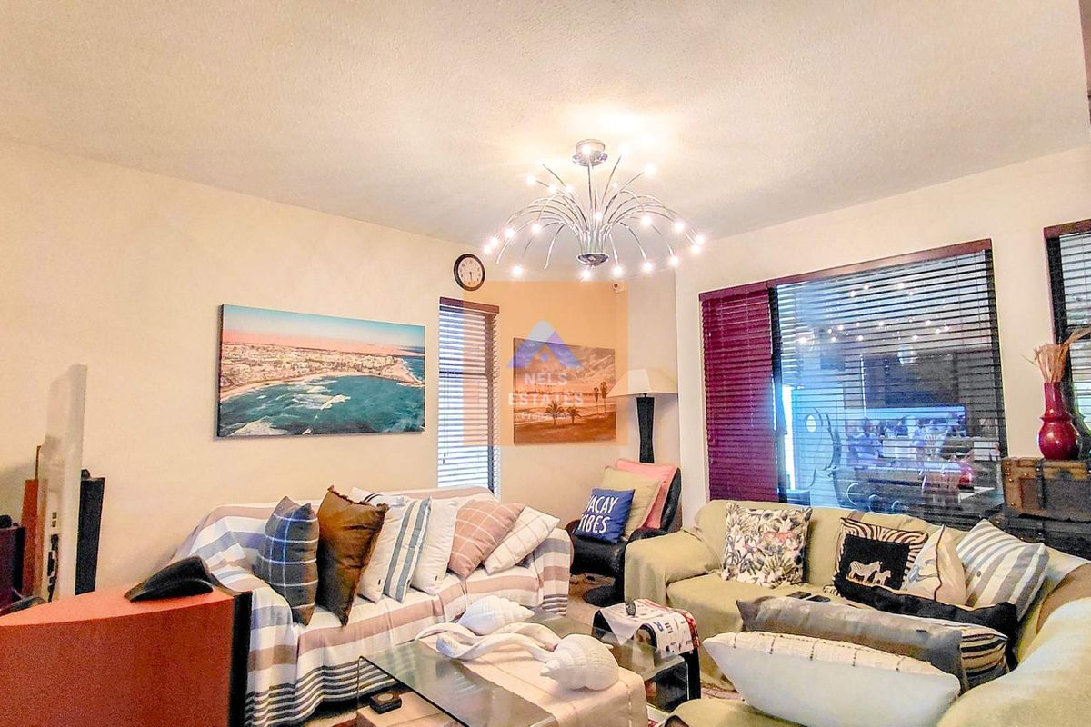 A comfortable living room featuring a modern chandelier, large windows with fitted blinds, and neutral wall finishes.