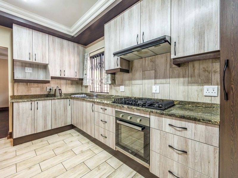 Modern kitchen featuring wood-look cabinetry, granite countertops, a gas hob, built-in oven, extractor fan, and tiled flooring.