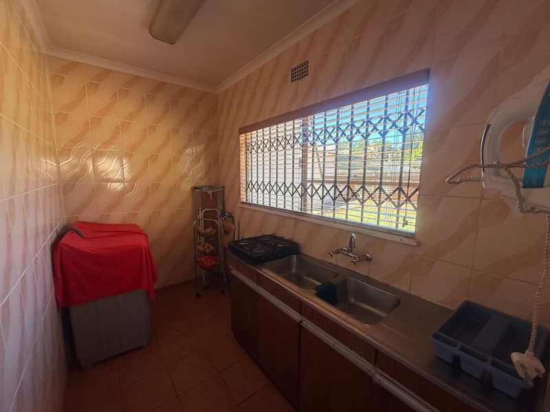 A functional kitchen featuring tiled walls, a double stainless steel sink, built-in cabinetry, and a gas cooktop with security bars on the window.