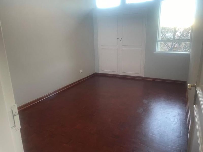 An empty bedroom featuring polished parquet flooring, built-in cupboards, and a window allowing natural light.