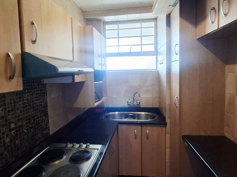 Compact kitchen featuring laminate cabinetry, granite countertops, a stainless steel double sink, electric hob, and extractor fan with tiled backsplash.