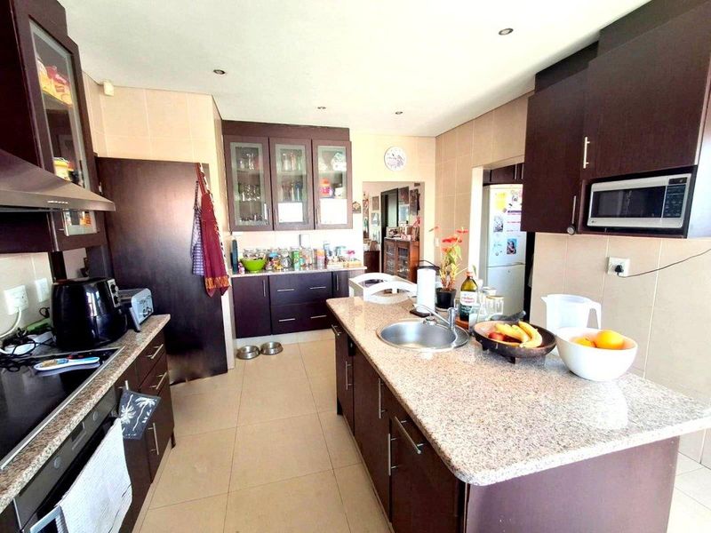 A functional kitchen featuring dark wood cabinetry, granite countertops, a central island with a sink, and integrated appliances including an oven and microwave.