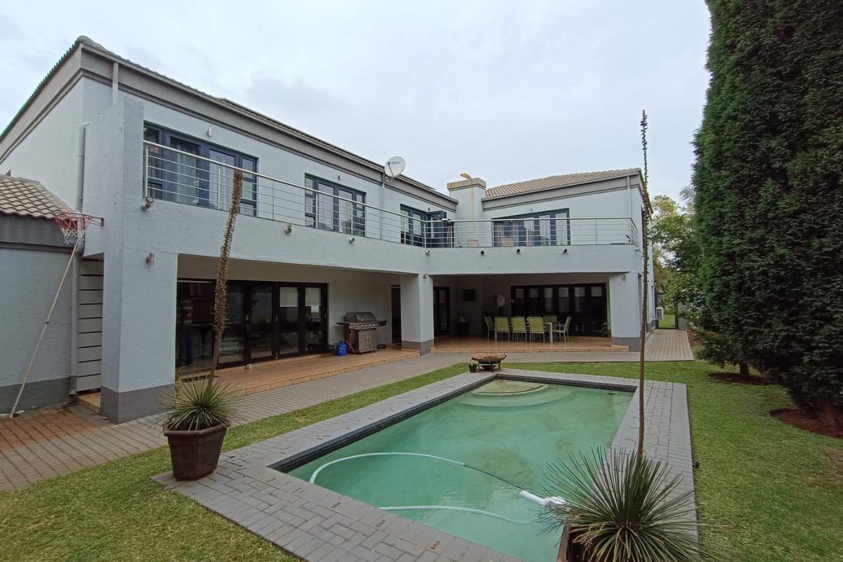 Spacious rear exterior featuring a swimming pool, paved patio area, and a two-story building with a balcony overlooking the garden.