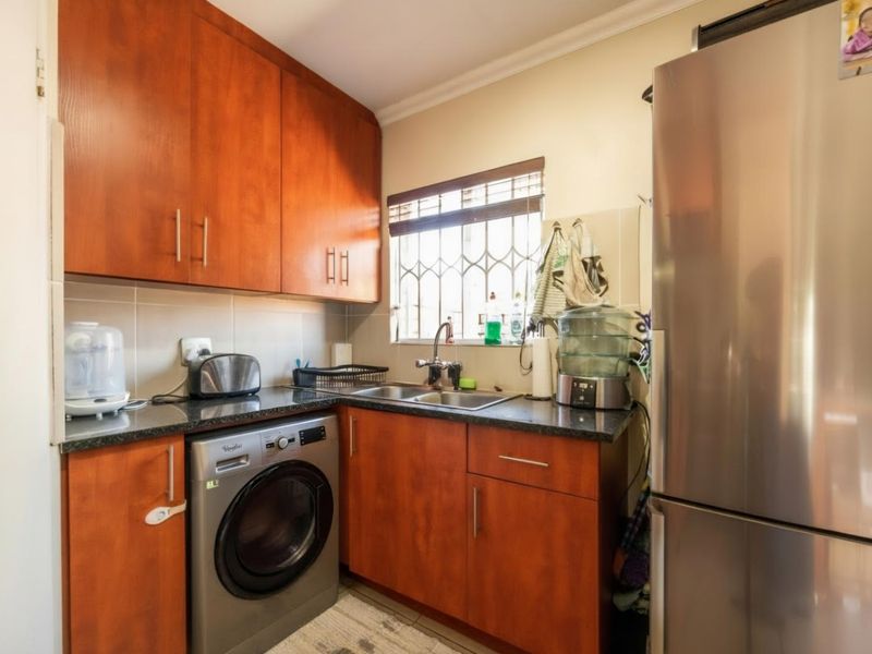 A compact kitchen featuring warm-toned laminate cabinetry, granite countertops, a stainless steel sink, and a tiled backsplash with security bars on the window.