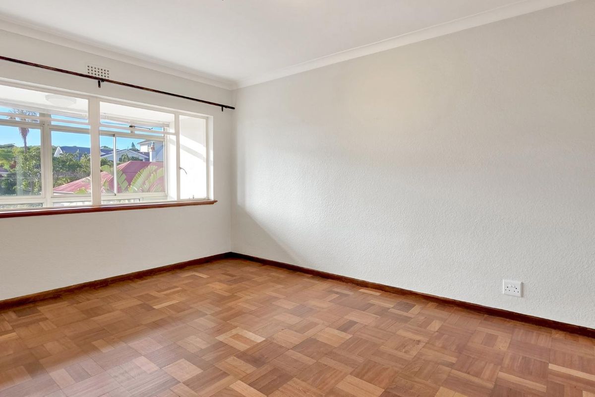 A bright, empty bedroom featuring classic parquet flooring, coved ceilings, and a large window providing natural light and neighborhood views.