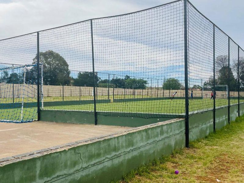 Outdoor sports facility featuring a fenced-in artificial turf pitch with integrated goal posts and concrete perimeter retaining walls.