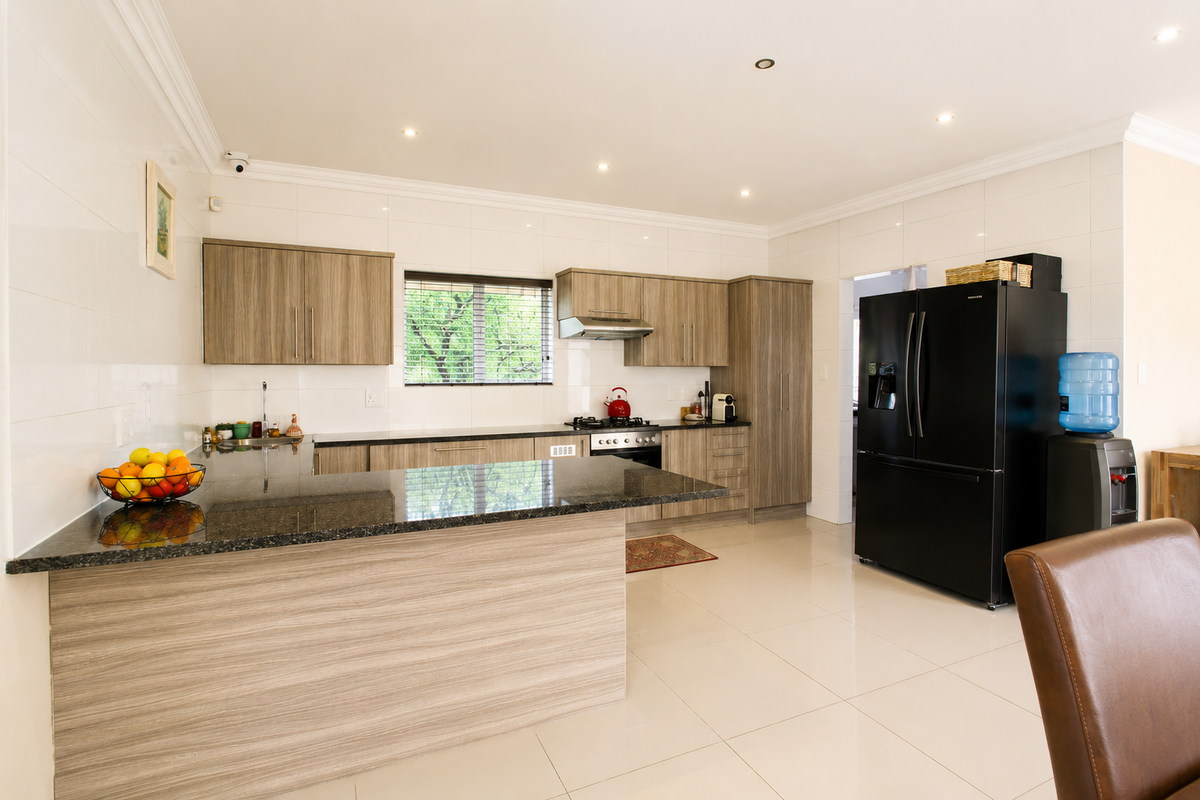 Modern kitchen featuring wood-grain cabinetry, granite countertops, a breakfast bar, and built-in stainless steel oven and extractor fan.