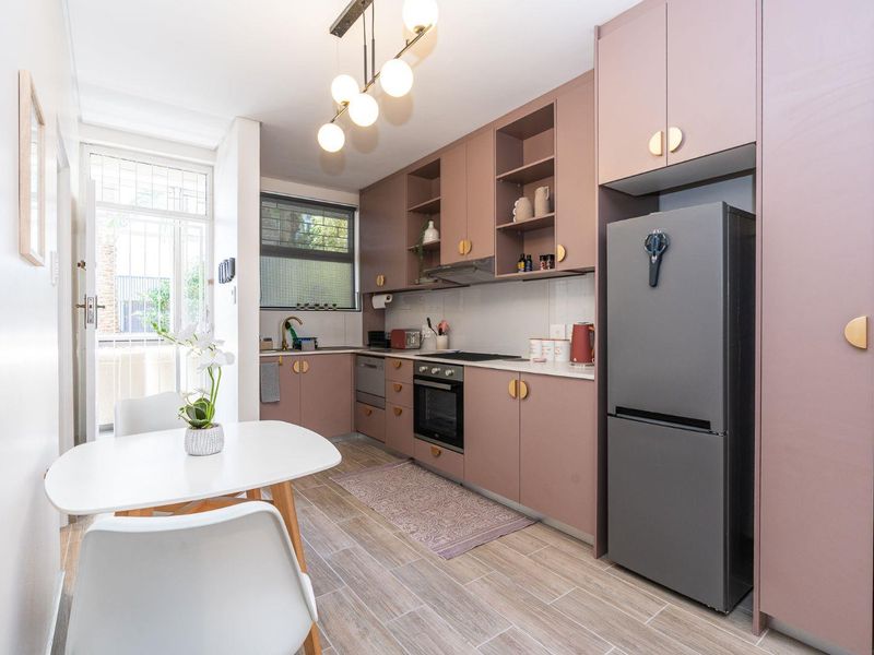 Modern kitchen featuring matte mauve cabinetry, integrated appliances, wood-look tiled flooring, and a functional layout with direct access to an outdoor area.