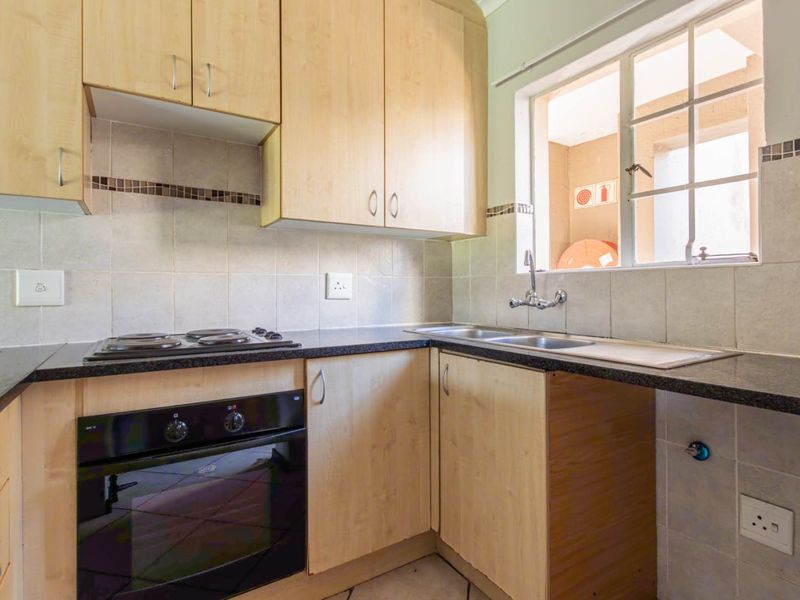A functional kitchen featuring light wood cabinetry, dark laminate countertops, a built-in oven, electric hob, and a double sink with tiled backsplash.