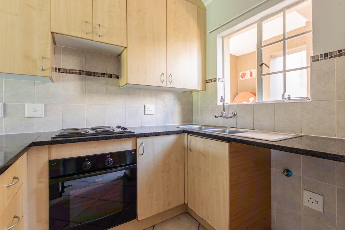 A functional kitchen featuring light wood cabinetry, dark laminate countertops, a built-in oven, electric hob, and a double sink with tiled backsplash.