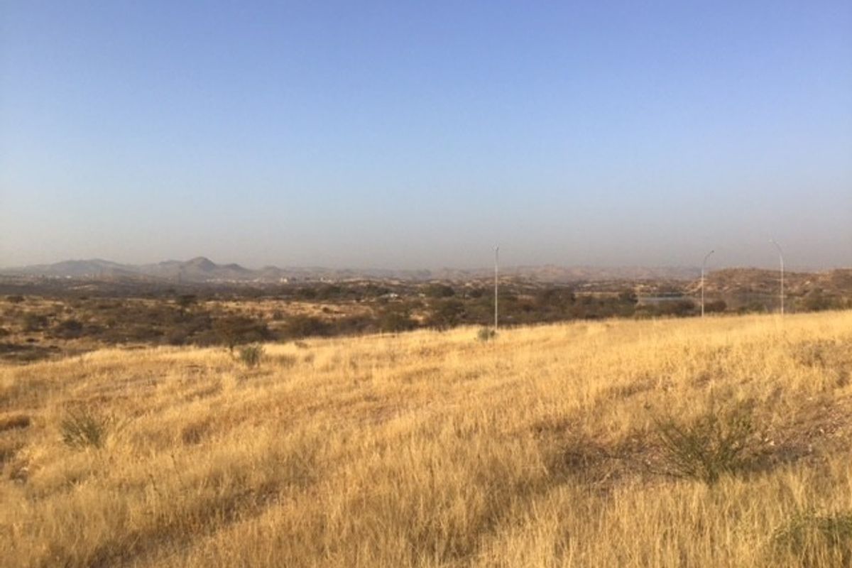 A wide-angle view of the vacant commercial land featuring dry grass and distant mountain landscape.