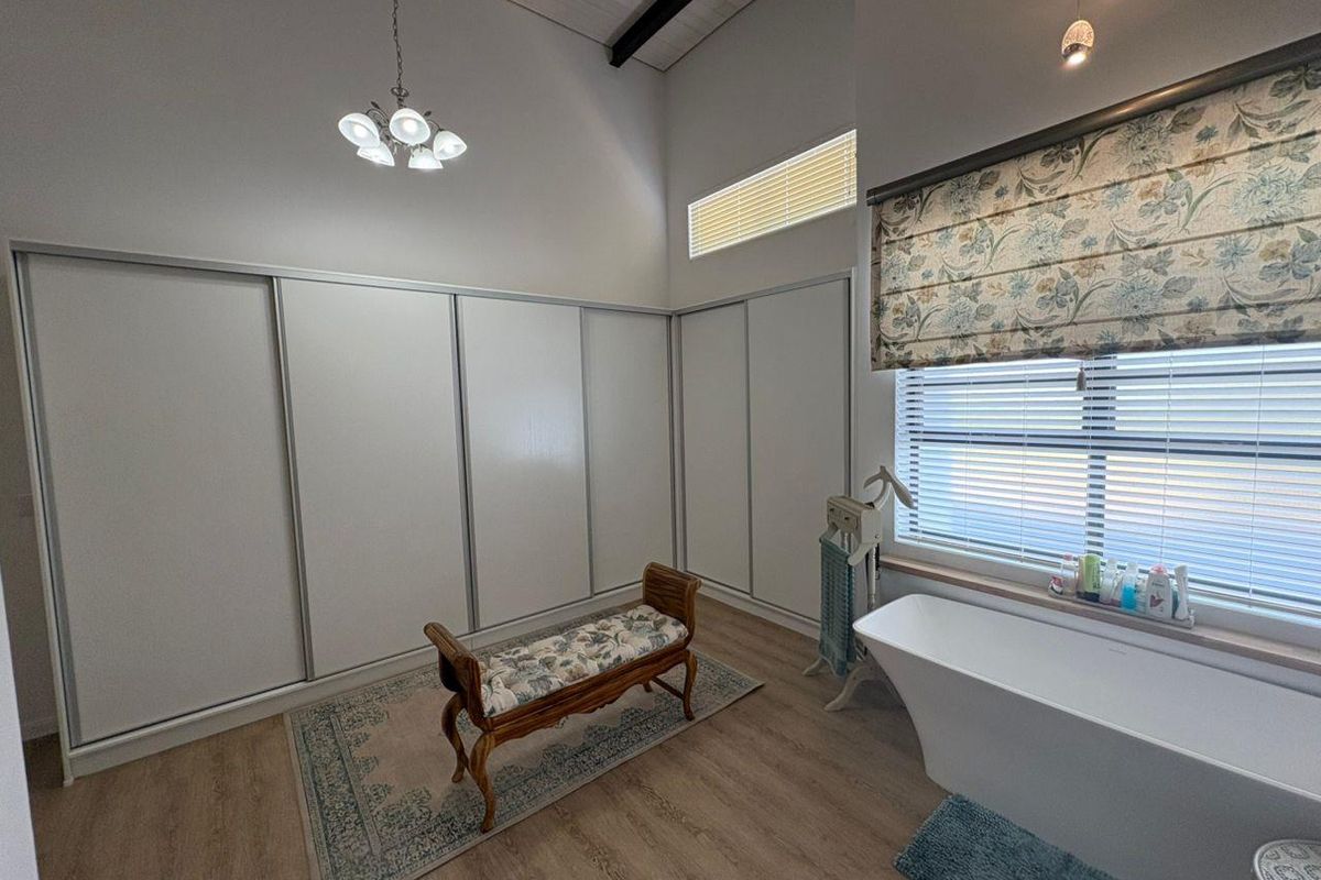 Spacious bathroom featuring high vaulted ceilings, built-in floor-to-ceiling sliding door wardrobes, and a modern freestanding bathtub positioned under a large window.