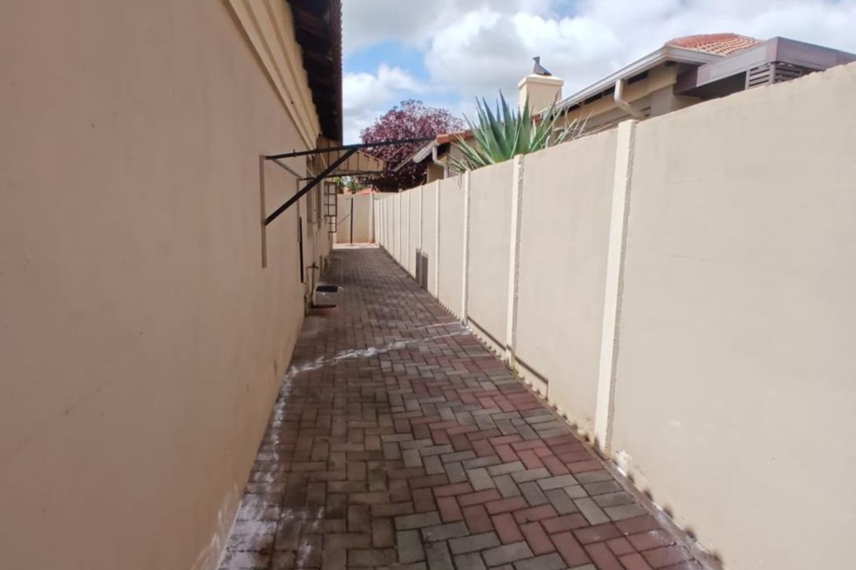 A narrow side passage featuring paved flooring and high boundary walls, providing a functional utility space along the side of the property.