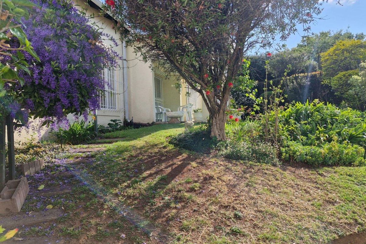 A view of the rear garden and exterior facade of the townhouse, featuring established trees, landscaped greenery, and a paved pathway.