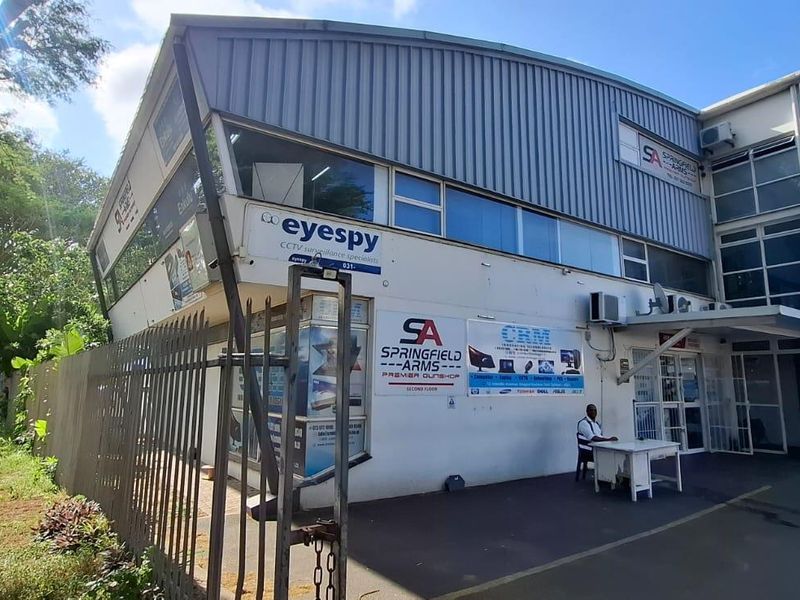 Front exterior view of a multi-tenant commercial building featuring metal roofing, aluminium windows, security fencing, and prominent business signage.