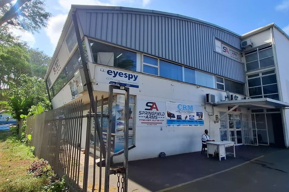 Front exterior view of a multi-tenant commercial building featuring metal roofing, aluminium windows, security fencing, and prominent business signage.