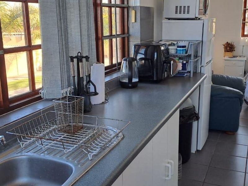 An open-plan studio apartment featuring a functional kitchenette with laminate countertops, stainless steel sink, and tiled flooring, seamlessly integrated with the sleeping area.