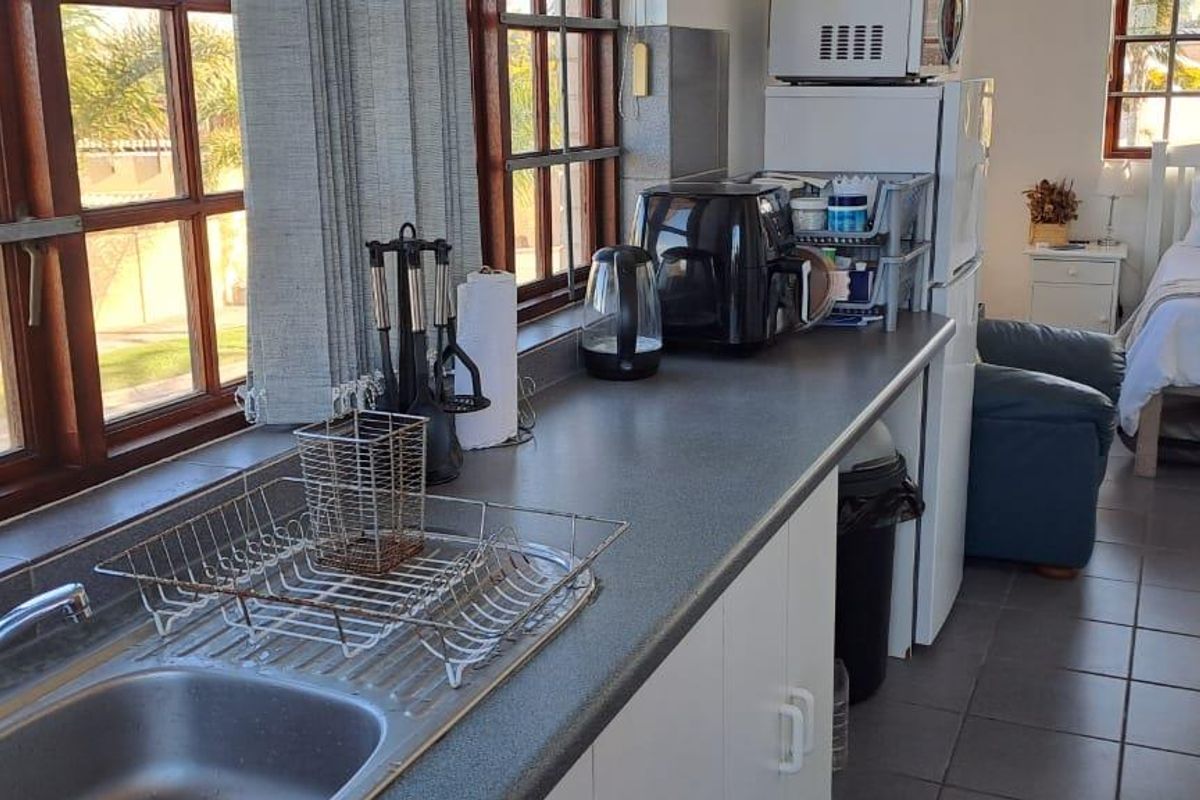 An open-plan studio apartment featuring a functional kitchenette with laminate countertops, stainless steel sink, and tiled flooring, seamlessly integrated with the sleeping area.