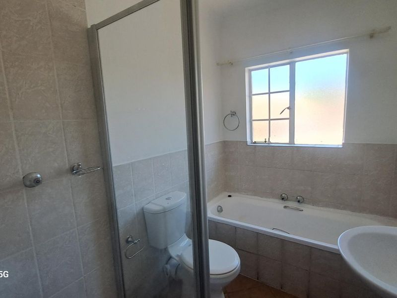 A functional bathroom featuring a shower enclosure, bathtub, pedestal basin, and toilet with neutral wall tiling and natural light from a window.