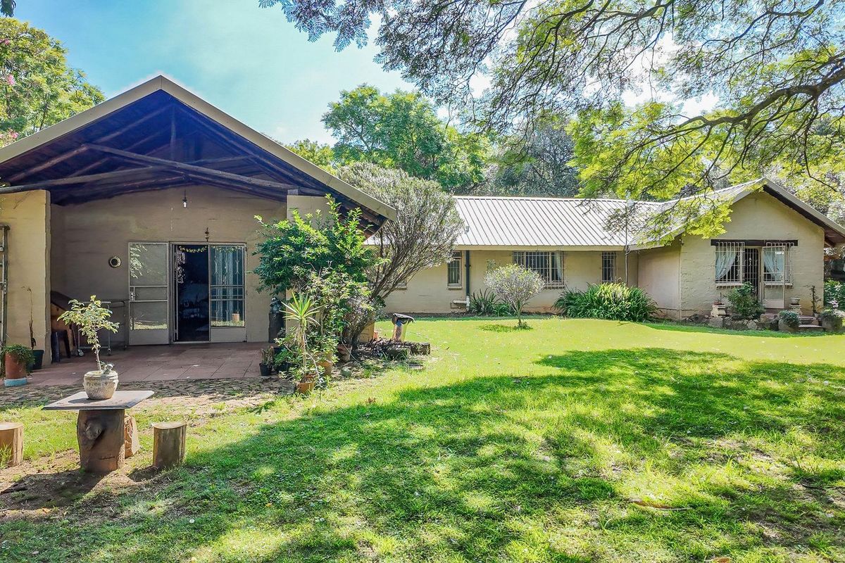 A spacious rear garden featuring a covered patio area, established trees, and a well-maintained lawn adjacent to the house exterior.