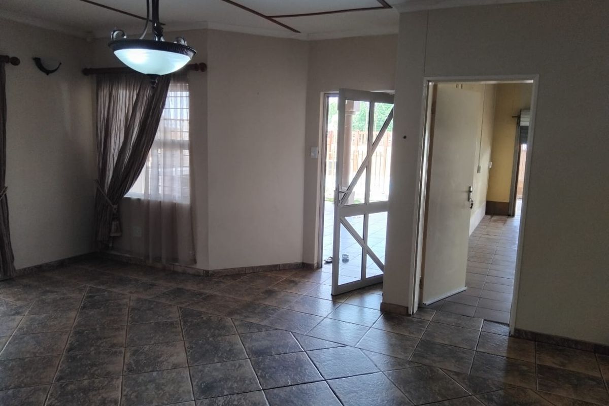A spacious living area featuring tiled flooring, a decorative ceiling light fixture, and direct access to an outdoor patio through a security gate.