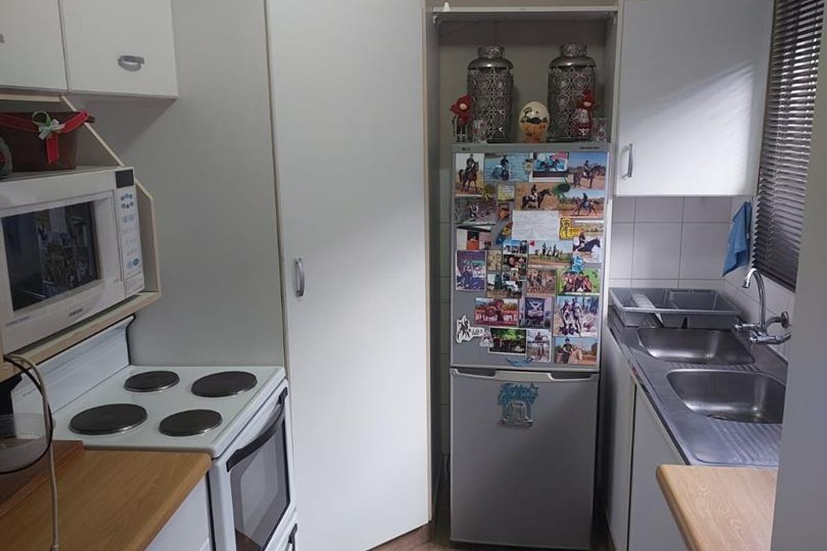Compact kitchen featuring white cabinetry, wood-look laminate countertops, a freestanding electric stove, and a double-basin stainless steel sink.