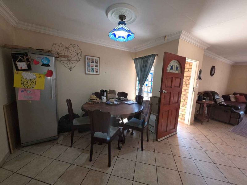 Open plan living and dining area featuring tiled flooring, decorative ceiling rose, and a timber entrance door.