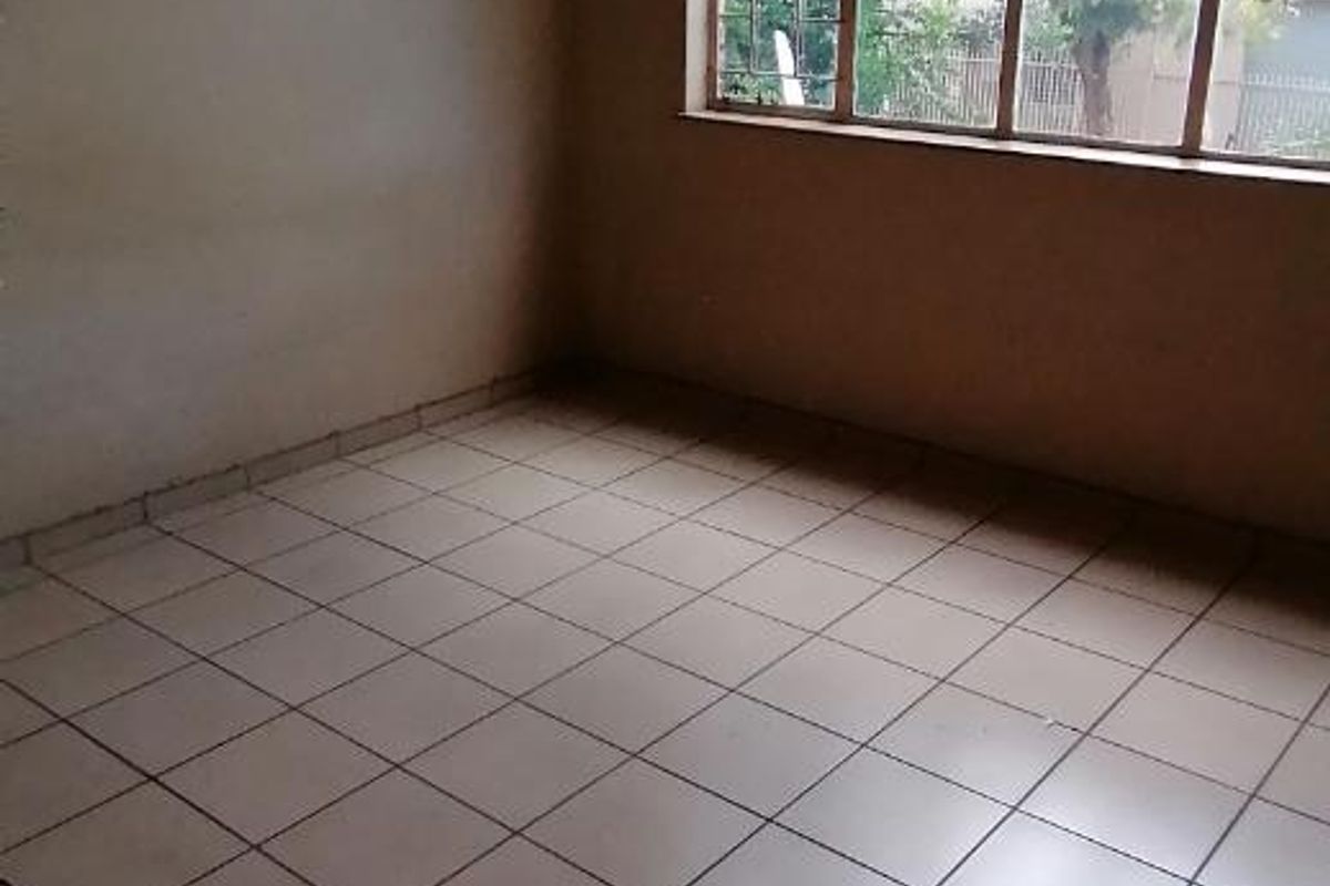 An empty bedroom featuring tiled flooring and a large window with security bars, offering a blank canvas for potential interior design updates.