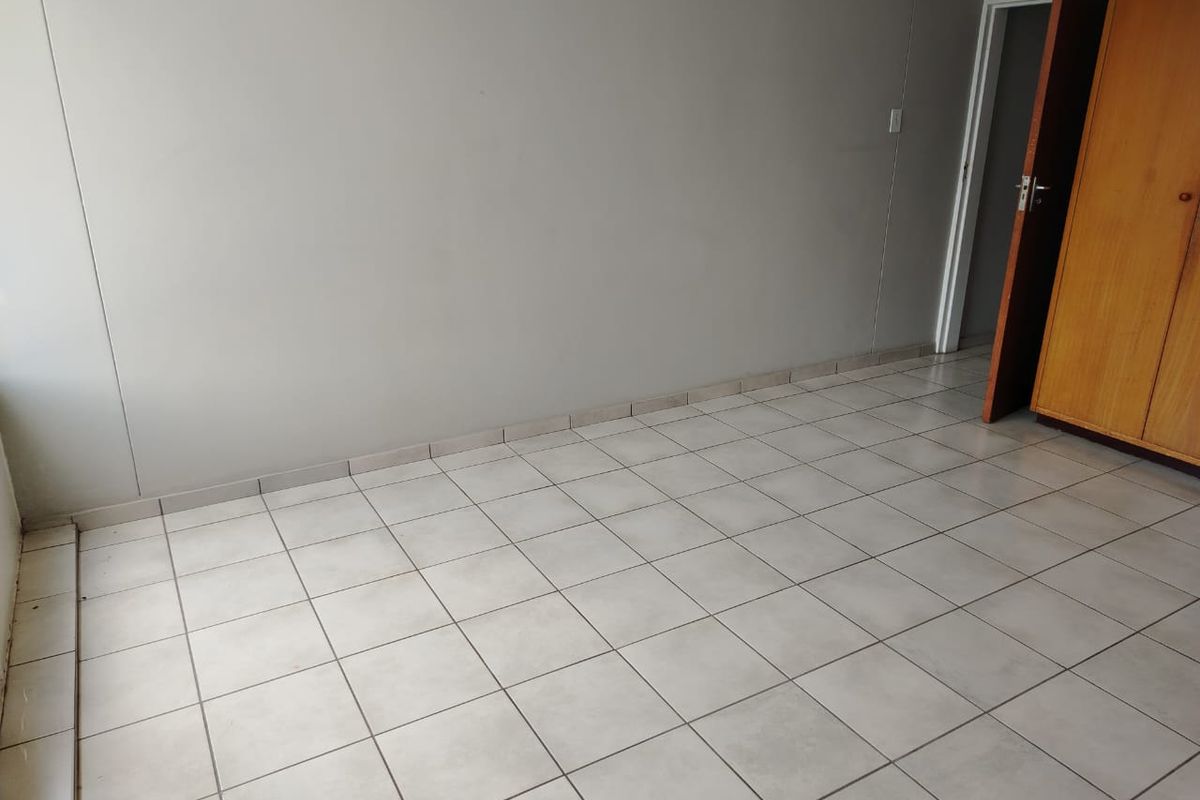 A simple, empty bedroom featuring neutral ceramic floor tiles and a built-in wooden wardrobe.
