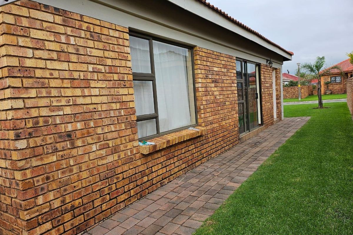 A view of the rear exterior featuring a face brick facade, paved walkway, and well-maintained lawn area.
