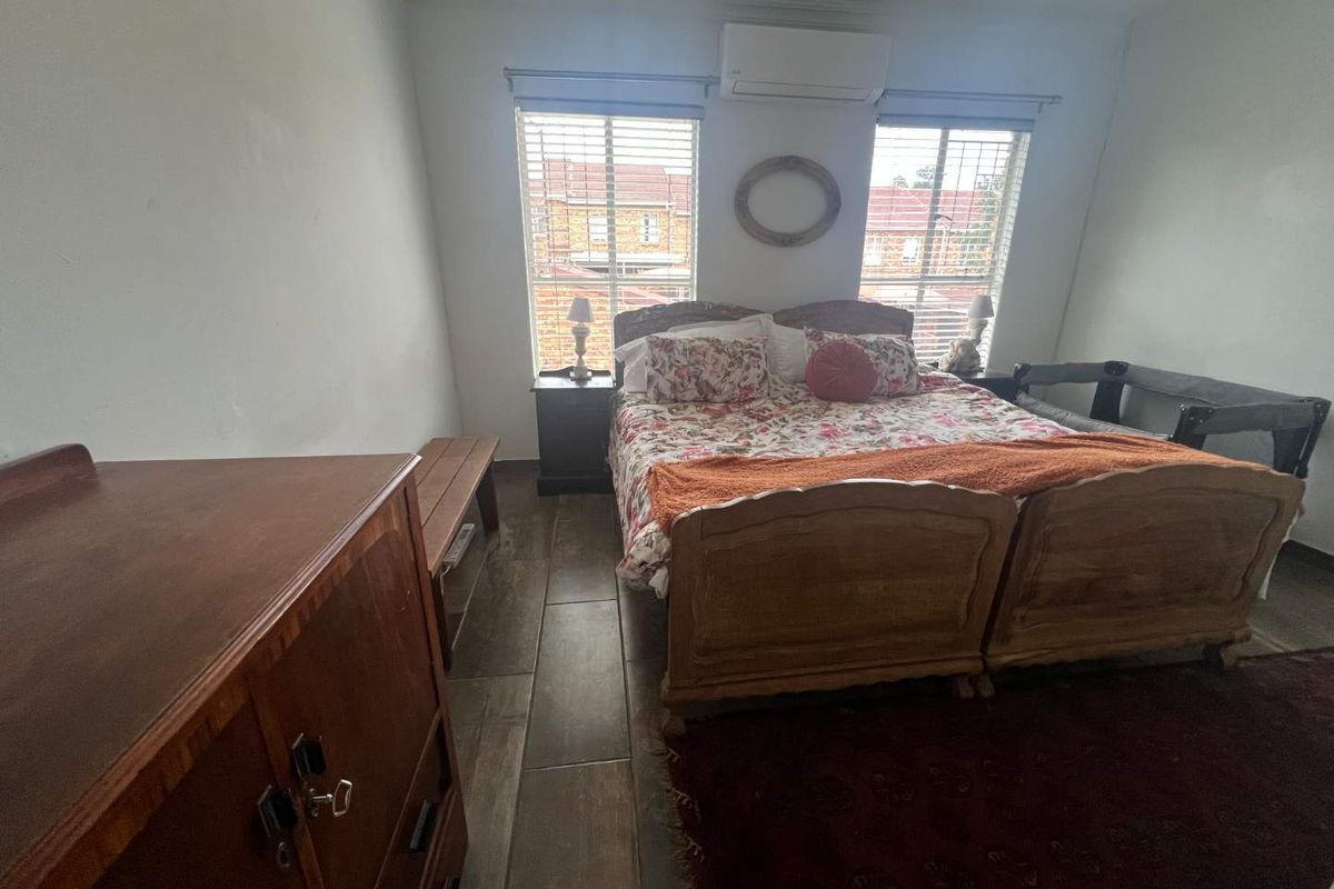 A bedroom featuring wood-look tile flooring, dual windows with blinds, and a wall-mounted air conditioning unit.