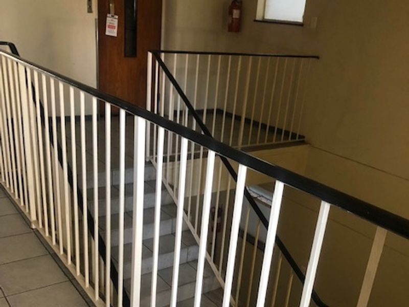 A functional apartment building stairwell featuring tiled flooring, metal safety balustrades, and an emergency exit door.