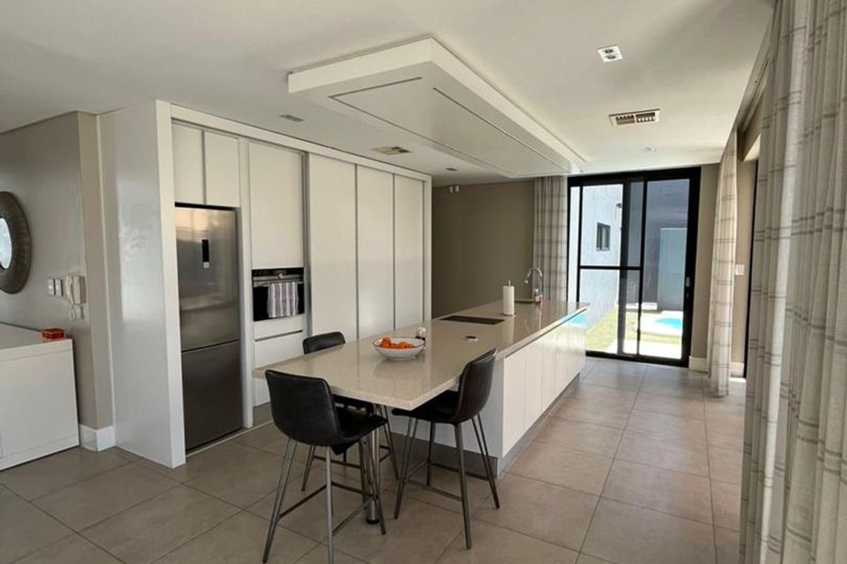 Modern kitchen featuring a large central island with stone countertops, integrated appliances, sleek cabinetry, and direct access to the outdoor pool area.