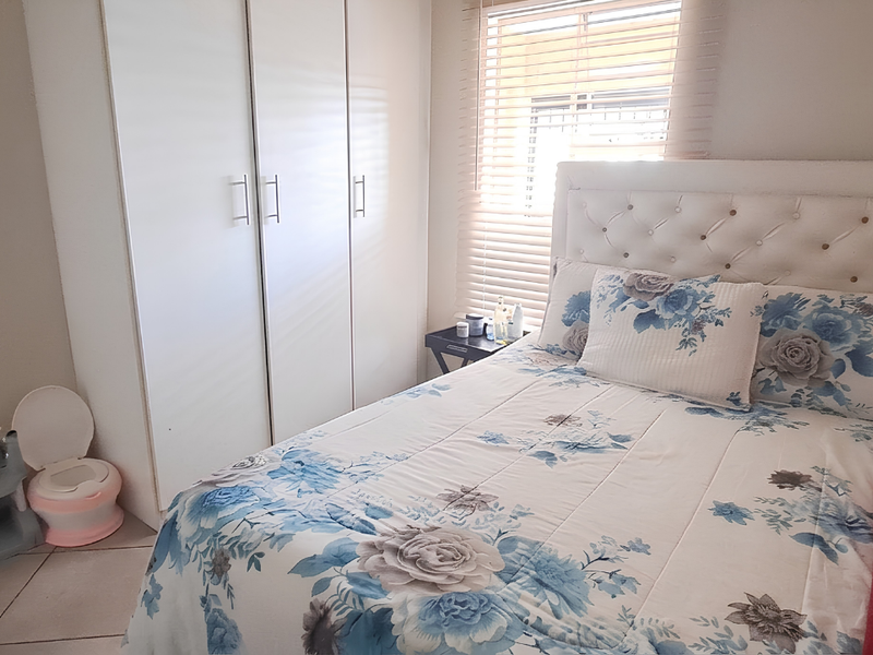 A functional bedroom featuring built-in cupboards, tiled flooring, and venetian blinds, providing a clean and practical living space.