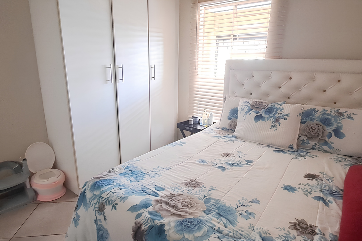 A functional bedroom featuring built-in cupboards, tiled flooring, and venetian blinds, providing a clean and practical living space.