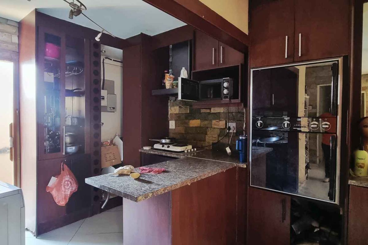 A dated kitchen featuring dark wood cabinetry, stone-look countertops, and a stone-clad backsplash with integrated appliances.