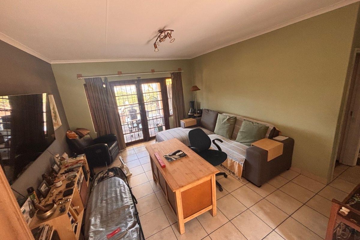 A living room featuring tiled flooring and double glass doors leading to an outdoor patio area.
