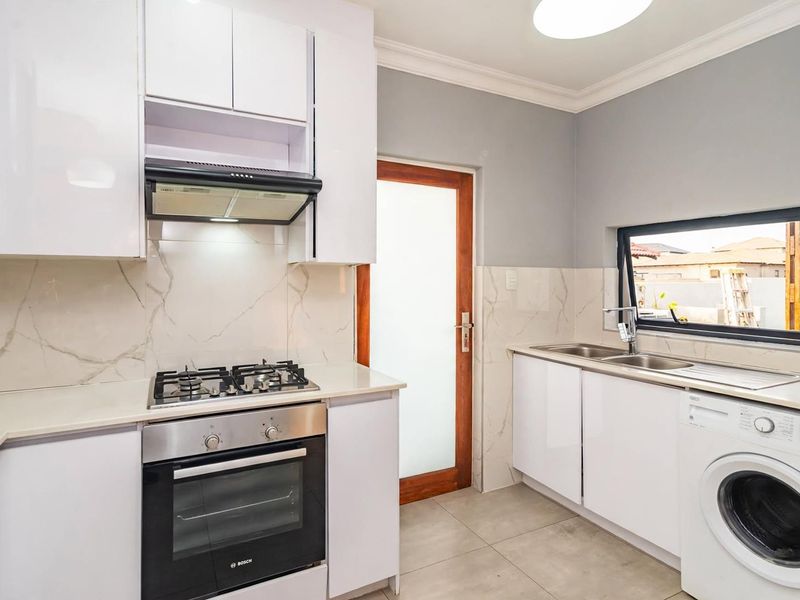 Modern kitchen featuring white gloss cabinetry, marble-look splashbacks, built-in gas hob, oven, extractor fan, and integrated laundry space with a double sink.