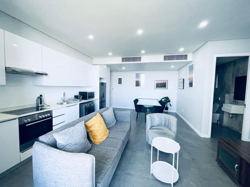 Modern open-plan living area featuring a sleek kitchen with built-in appliances, recessed lighting, and ducted air conditioning, seamlessly flowing into the dining and lounge space.