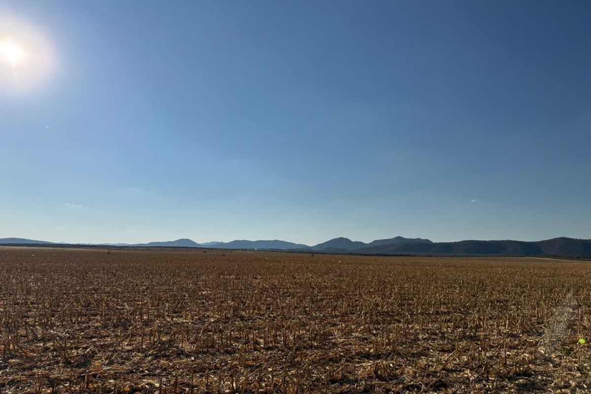 Expansive view of open farmland with distant mountain ranges under a clear blue sky.