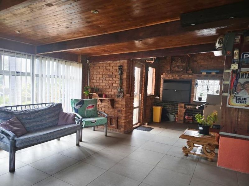 Covered patio area featuring a rustic exposed timber ceiling, tiled flooring, and a built-in brick fireplace, ideal for outdoor entertaining.