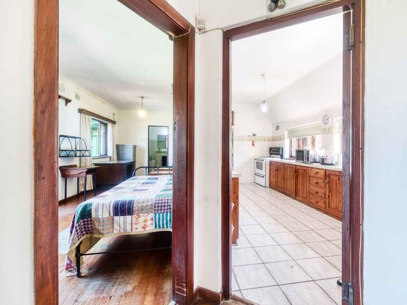 View from a hallway looking into a bedroom with timber floors and a kitchen featuring wooden cabinetry and tiled flooring.
