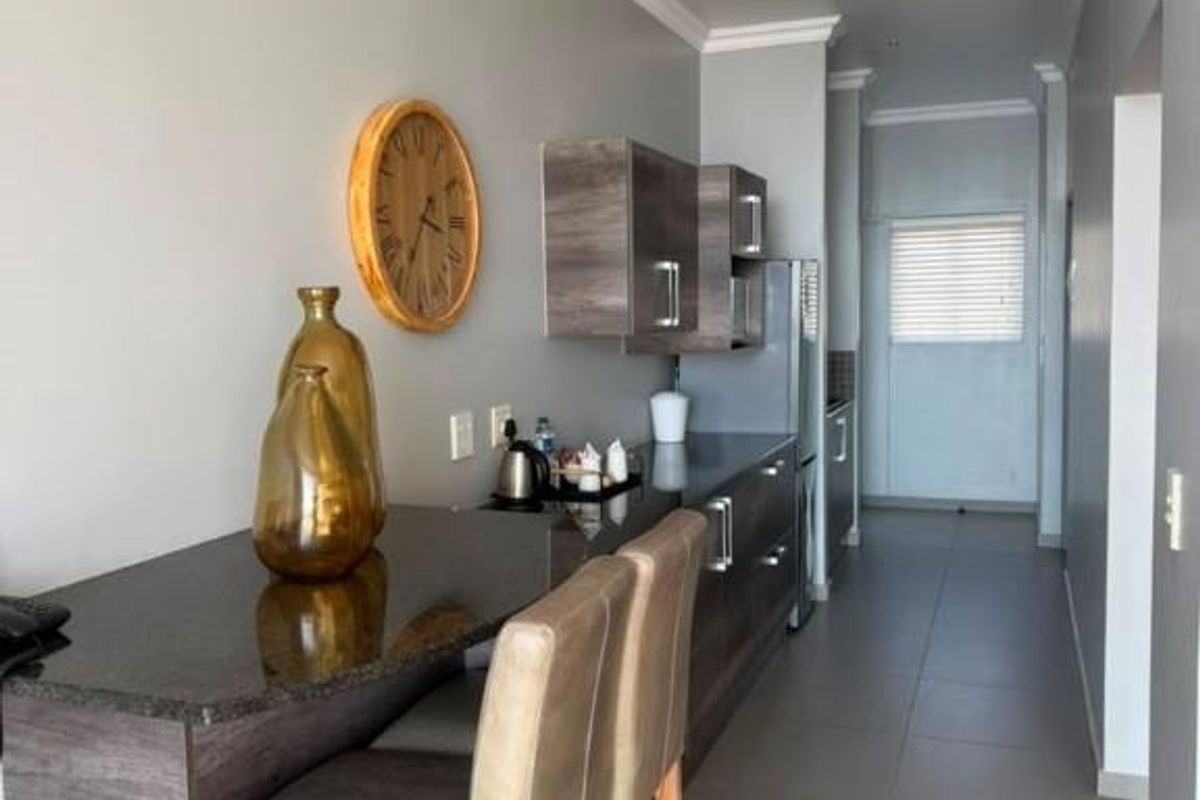 Modern kitchen featuring sleek dark cabinetry, granite countertops with an integrated breakfast bar, and neutral tiled flooring in a well-lit, open-plan layout.