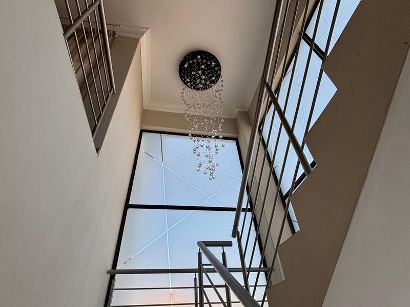 A bright, modern stairwell featuring a large architectural window, stainless steel balustrades, and a contemporary crystal chandelier.