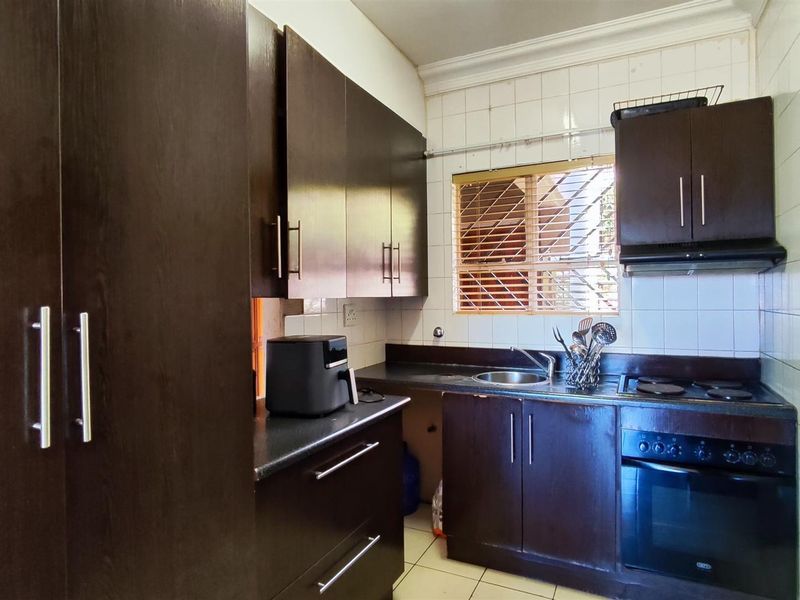 A compact kitchen featuring dark wood cabinetry, built-in oven with hob, extractor fan, and tiled splashbacks, offering a functional layout for daily meal preparation.