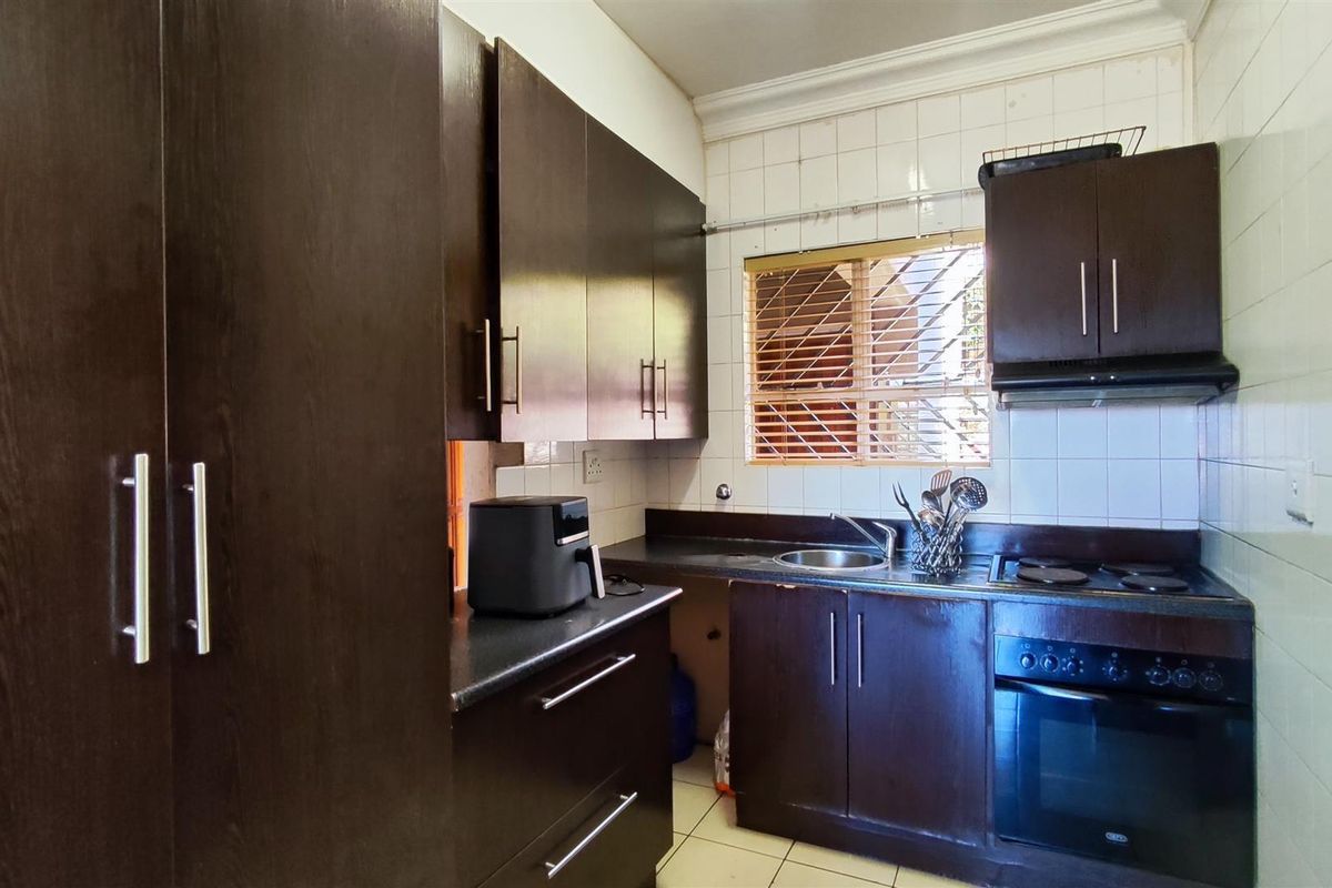 A compact kitchen featuring dark wood cabinetry, built-in oven with hob, extractor fan, and tiled splashbacks, offering a functional layout for daily meal preparation.